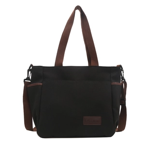 Minimalist black canvas tote bag with brown straps and side pockets on white background