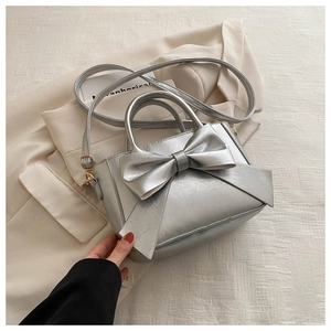 Detail of silver metallic textured crossbody bag with oversized bow and top handles