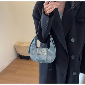 Close-up of blue washed denim crescent bag with gold buckle and tassel detail