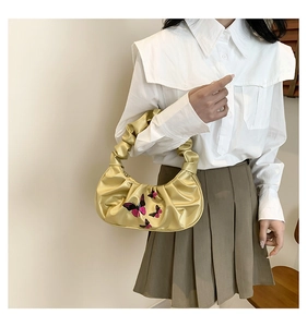 Detail of metallic gold pleated handbag featuring purple butterfly print and ruched handle