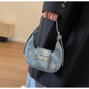 Detail shot of washed blue denim crescent bag with gold metal buckle and leather strap