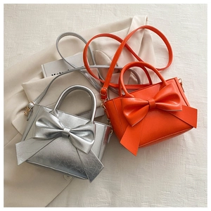 Detail of trendy bow handbags in silver metallic and vibrant orange with top handles