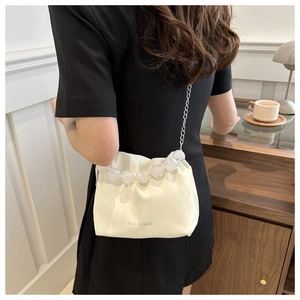 Détail du sac seau crème avec poignée en perles et chaîne argentée sur le mannequin