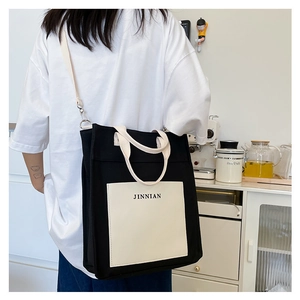 Detail of minimalist black canvas tote bag with contrast pocket and JINNIAN logo