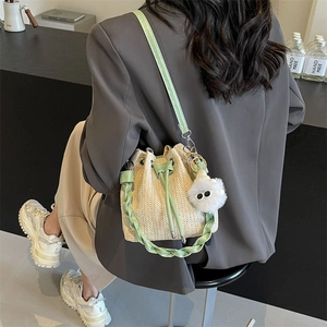 Woven straw bucket bag with green faux leather strap and decorative plush pom-pom charm