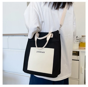 Detail of minimalist black and white canvas tote with JINNIAN logo and wide shoulder strap