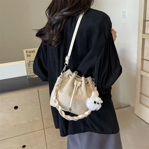 Beige woven straw bucket bag with plush charm and stylish braided handle for beach