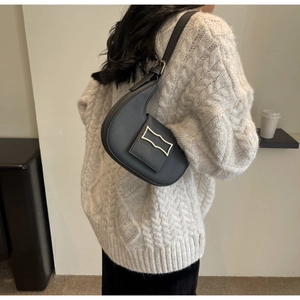 Detail of black matte crescent bag with gold metal clasp on a model in a white sweater