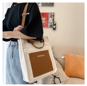 Close-up of canvas tote bag featuring brown leather pocket and adjustable shoulder strap