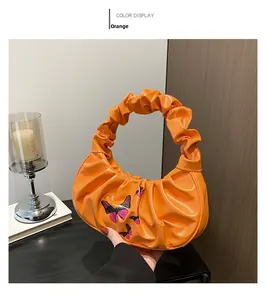 Detailed view of an orange ruched cloud bag with pink butterfly prints and handle details