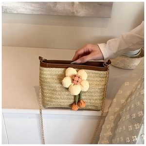 Détail du sac seau en paille avec breloque fleurie et bandoulière dorée