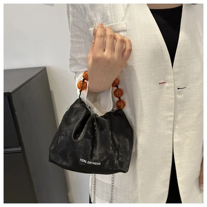 Détail du sac seau noir avec poignée en perles ambrées et bandoulière argentée