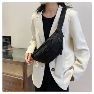 Close-up of black quilted waist bag with geometric texture and dual zippers on white blazer
