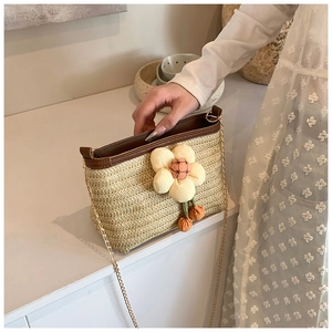 Gros plan détaillé du sac seau en paille tressée avec breloque fleur et chaîne dorée
