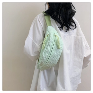 Detail of light green chest bag showing textured embossed fabric and woven strap