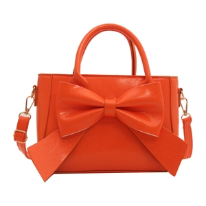 Orange structured handbag with a large bow detail and gold hardware on white background