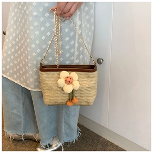Détail du sac seau en paille tressée avec fleurs décoratives et bandoulière en chaîne dorée