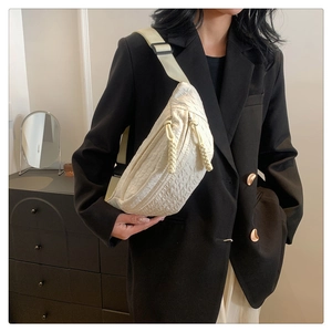 Close-up of beige textured fabric crossbody bag with braided zipper pulls on a model