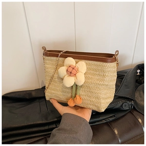 Détail d'un sac seau en paille tressée avec une grande fleur en peluche et chaîne dorée