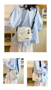 Détail d'un sac bandoulière en toile blanche avec étiquette mode et poche zippée biais