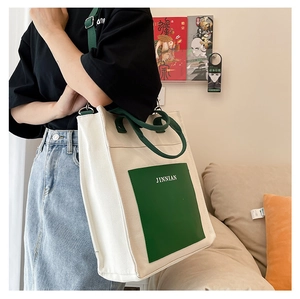Detail view of large white canvas tote bag with green leather pocket and carry handles