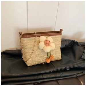 Détail du sac seau en paille tressée avec fleur en peluche rose et bandoulière dorée
