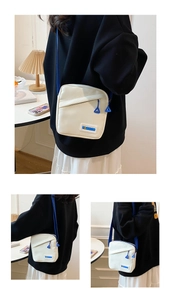 Détail d'un sac bandoulière en toile crème avec accents bleus et étiquette de mode