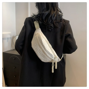 Detailed macro view of beige textured chest bag with woven rope zipper pullers