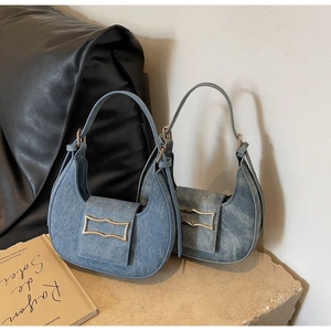 Detail of two blue denim crescent handbags with gold buckles on a stone display stand