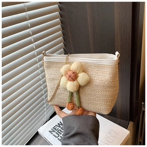 Détail du sac seau en paille tressée avec breloque florale et bandoulière en chaîne dorée