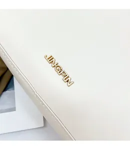 Dettaglio borsa in pelle avorio con logo metallico dorato JINGPIN in rilievo 3D