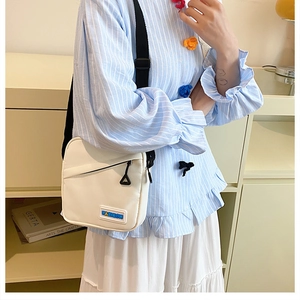 Détail d'un sac bandoulière en toile blanche avec sangle noire et étiquette bleue tendance