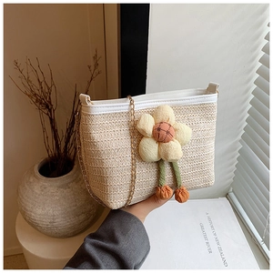 Détail du sac seau en paille tressée beige avec breloque fleurie et chaîne dorée