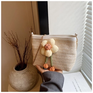 Détail du sac seau en paille tressée avec une grande fleur en peluche et chaîne dorée