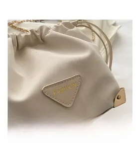 Macro detail of creamy white leather bucket bag with gold chain and triangle metal logo