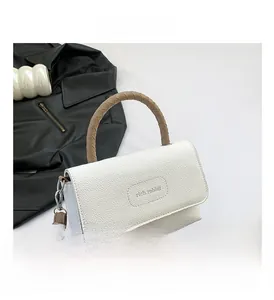 Détail d'un sac à main en cuir grainé blanc avec poignée tressée marron et logo sur rabat