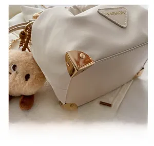 Detail of off-white leather bucket bag featuring metal corner protectors and a cute plush charm