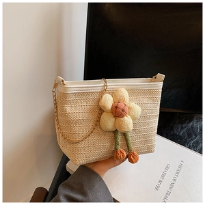 Détail du sac seau en paille couleur avoine avec grande fleur en tissu et chaîne dorée