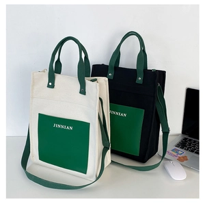 Detail of canvas tote bag showing front pocket with JINNIAN logo and green fabric handles