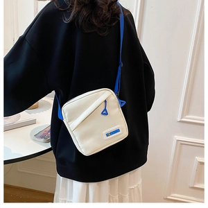 Détail du sac à bandoulière en toile crème avec sangle bleue et broderie fashion sur le devant