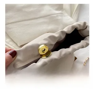 Detailed close-up of golden cylindrical magnetic clasp on off-white bucket bag