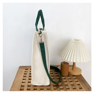 Detailed side view of canvas tote bag with green straps on a wooden shelf