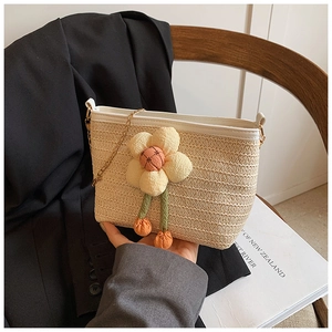 Gros plan détaillé du sac seau en paille tressée avec fleur 3D et bandoulière chaîne dorée