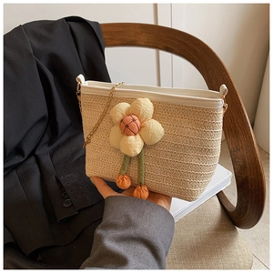 Détail du sac seau en paille tressée avec fleur décorative et bandoulière en chaîne