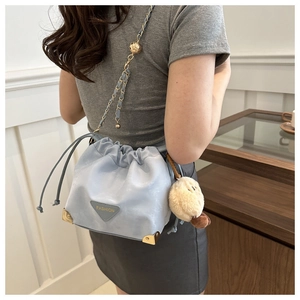 Detail of light blue bucket bag with gold corners, chain strap, and cute plush charm