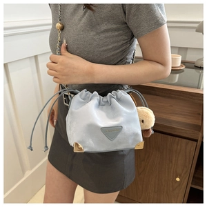 Detail of light blue bucket bag with gold corners, metal chain and plush charm