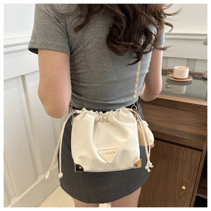 Detail of cream white bucket bag with gold chain strap, drawstring closure and metal corners