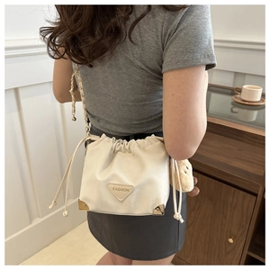 Detail of a creamy white drawstring bucket bag with gold chain strap and metal corners