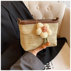 Détail du sac seau en paille tissée avec breloque fleur en peluche et chaîne dorée