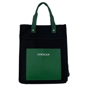 Detail of the JINNIAN logo on a black canvas tote with deep green woven handles
